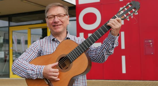 Thomas Mertin, der neue Leiter der Musikschule Hoyerswerda, steht mit einer Gitarre vor der Einrichtung.